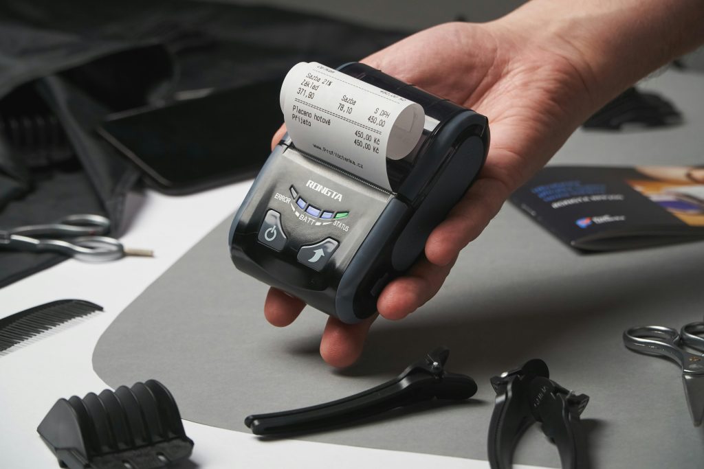 Close-up of a hand holding a digital printing device with a receipt, surrounded by grooming tools.